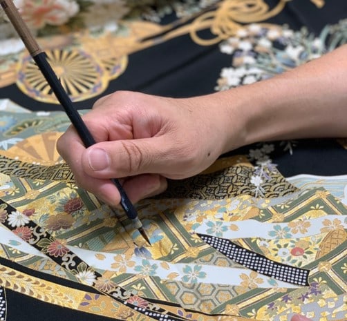 筆を使って着物の金彩を補修する職人の手元